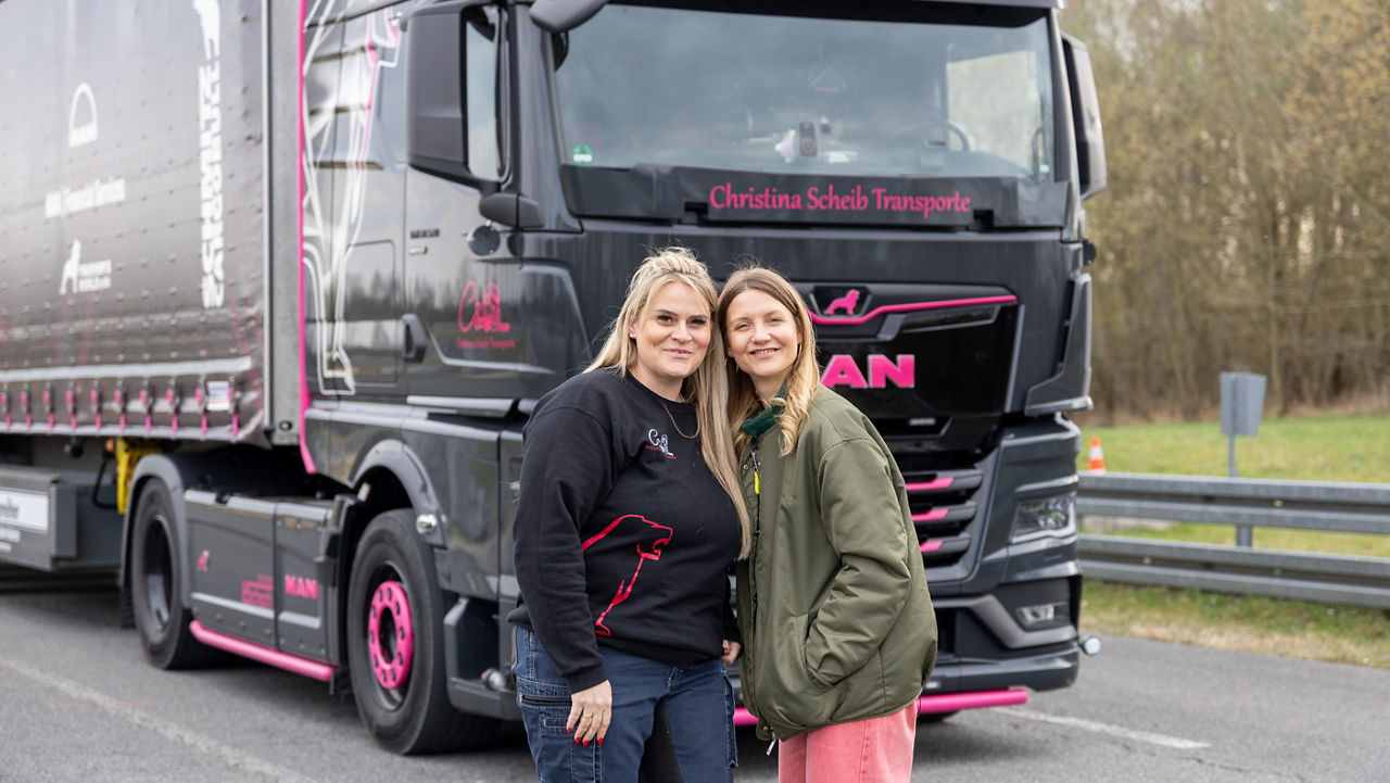 Christina Scheib mit Jana Forkel vor ihrem schwarzen MAN TGX mit pinken Zierelementen und herkömmlichen Lkw-Spiegel.